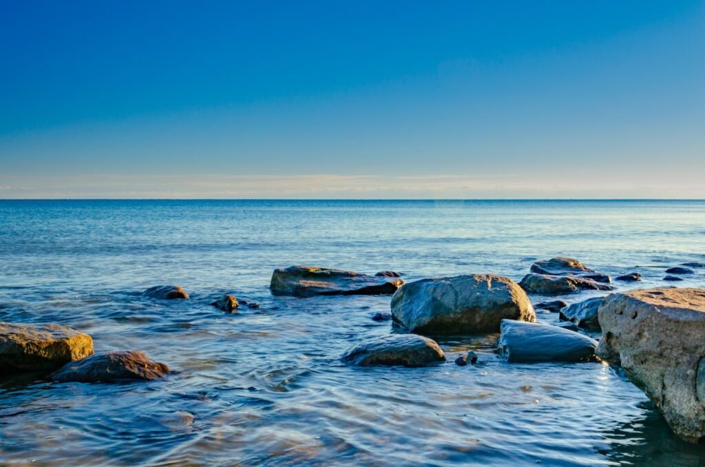 Rocks On Body Of Water Under Blue Sky