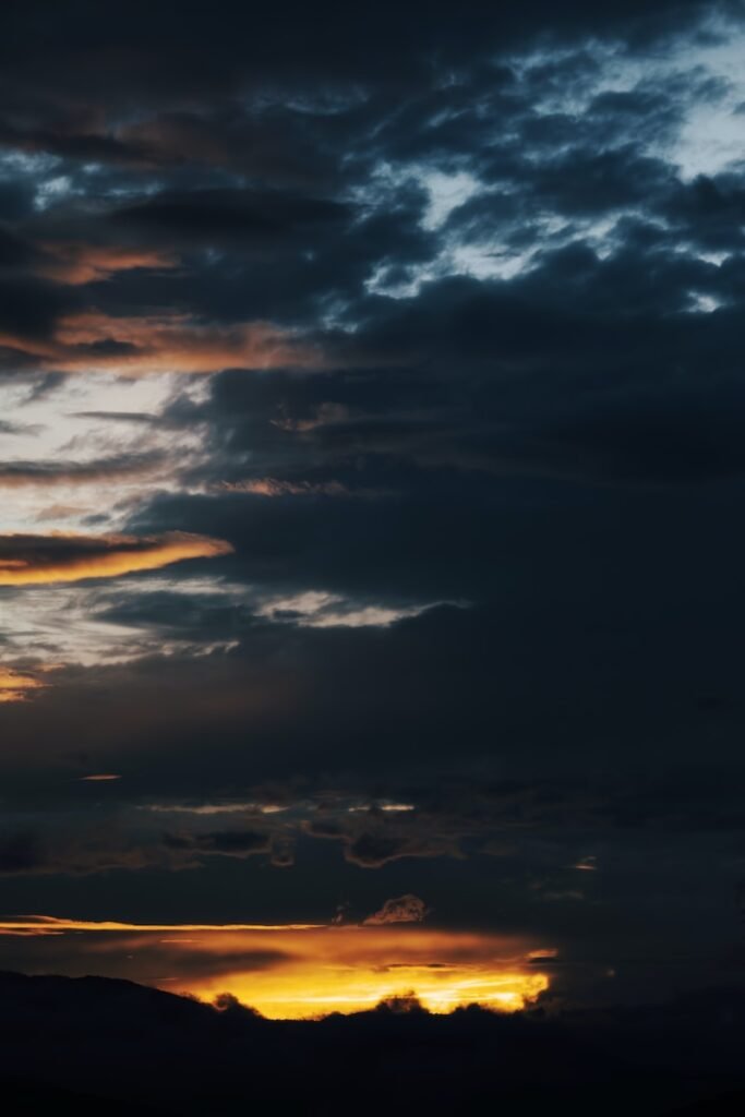 a plane flying through a cloudy sky at sunset