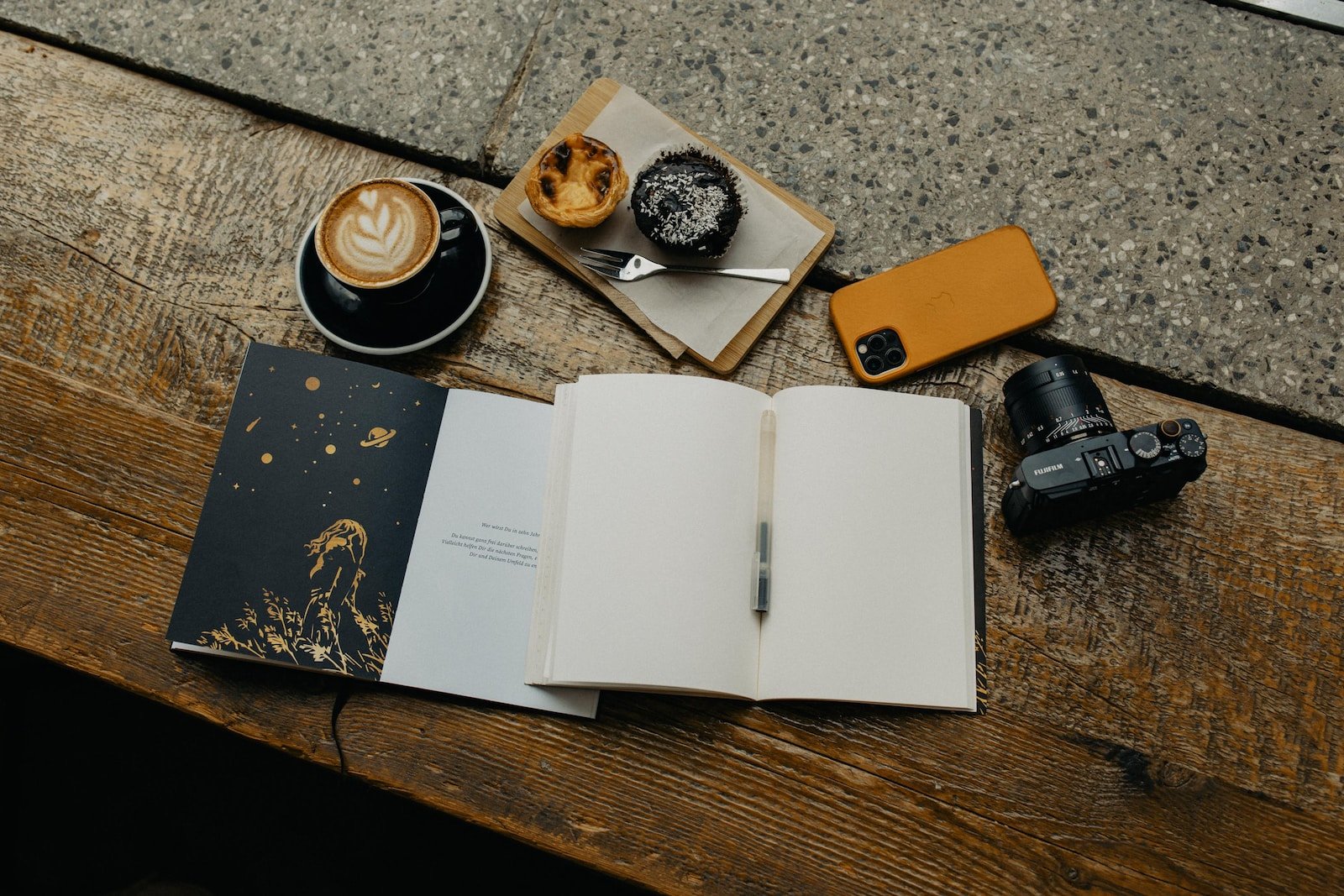 an open book sitting on top of a wooden table next to a cup of coffee