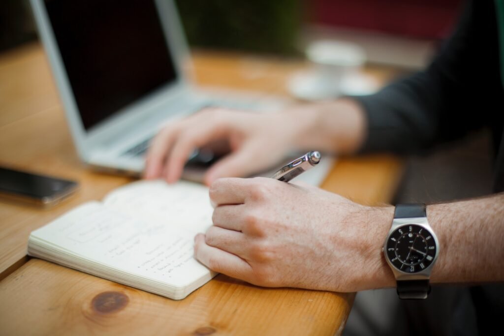 man sitting while writing on notebook